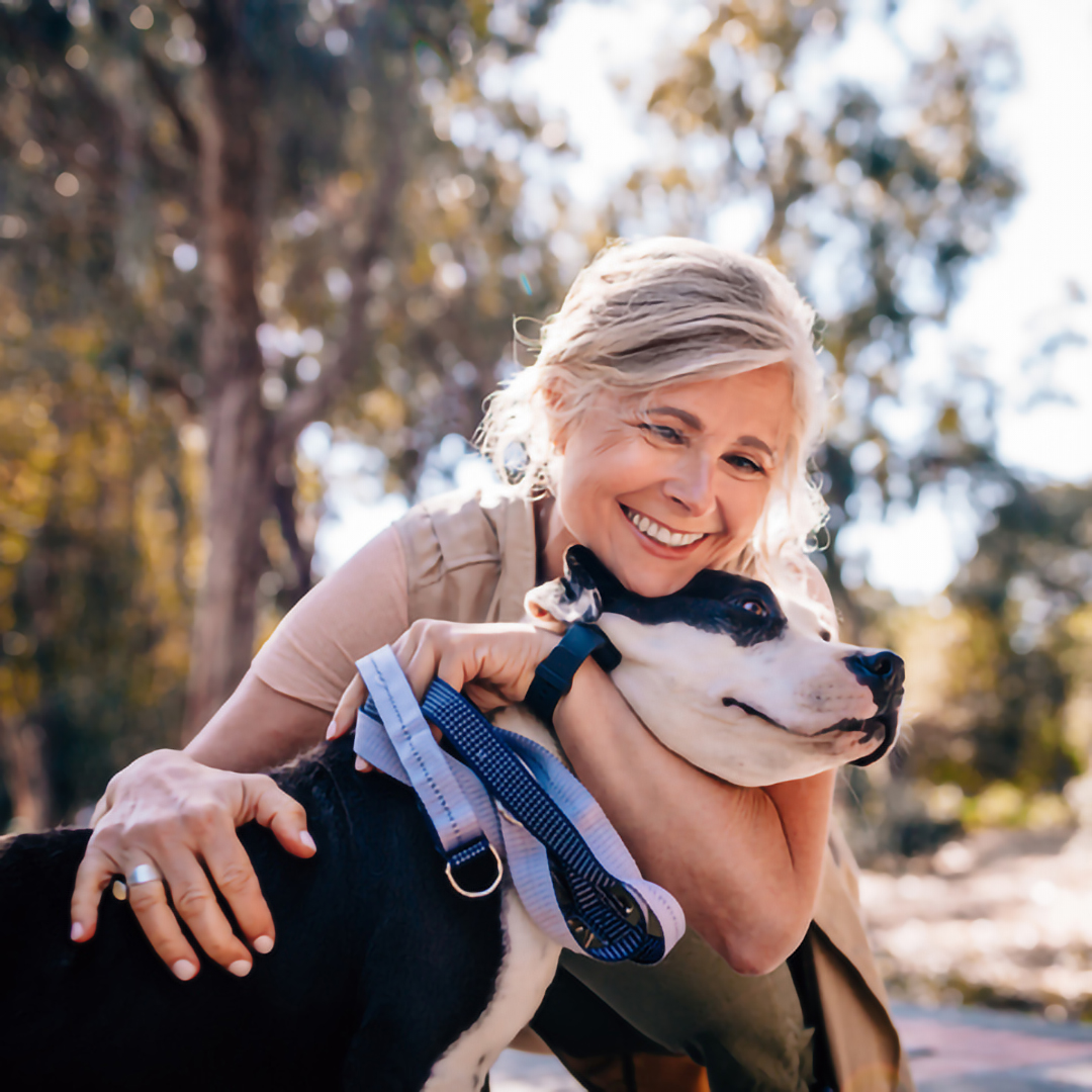 An older woman hugs her dog while taking a walk outside.
