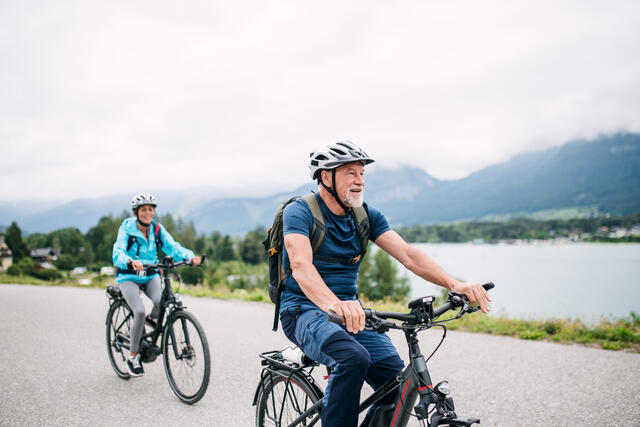 two people ride bikes next to a natural body of water