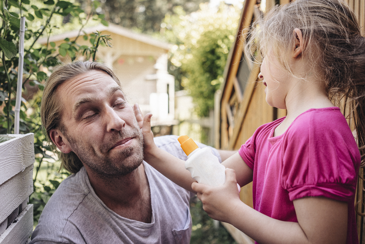 Child applying sunscreen to adult’s face to protect against UV rays