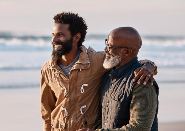 A young man and his father enjoy walking along the beach at sunset.