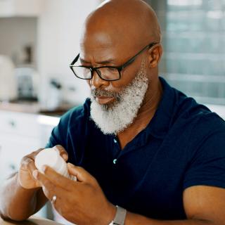 A man reads a medication label at his kitchen table.