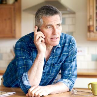 A man talks to a pharmacist on his phone from his kitchen.