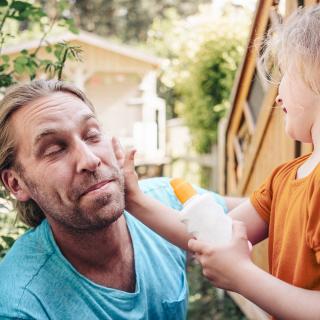 A young girl applies sunscreen to her father’s face.